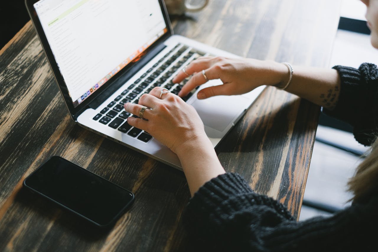 From above of anonymous female freelancer browsing internet on netbook while sitting at wooden table with smartphone during remote work